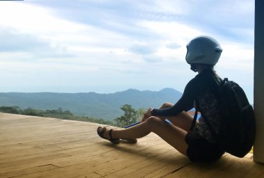 Motosiklet kasklı, dağlarda oturup izleyen çekici genç kadın. Koh Samui. Tayland