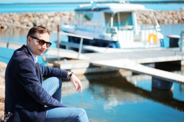 Yaz tatilinde lüks bir yatın önünde poz veren güneş gözlüklü yakışıklı bir erkek model. Boşluğu kopyala