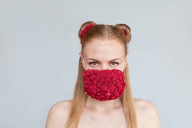 Beyaz arka planda kırmızı çiçekleri olan koruyucu tıbbi maskeli güzel bir kadın. Kapsamlı koruma - 19.