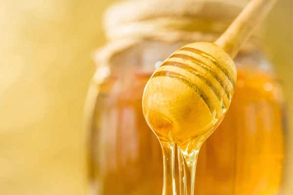 A honey spoon against the background of a jar filled with honey — Stock Photo, Image