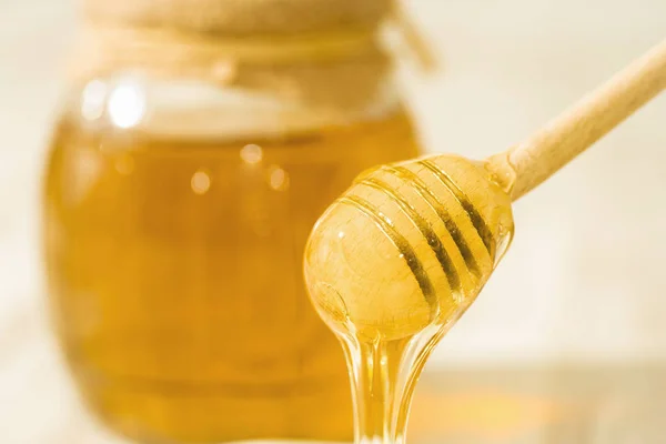 A honey spoon against the background of a jar filled with honey — Stock Photo, Image