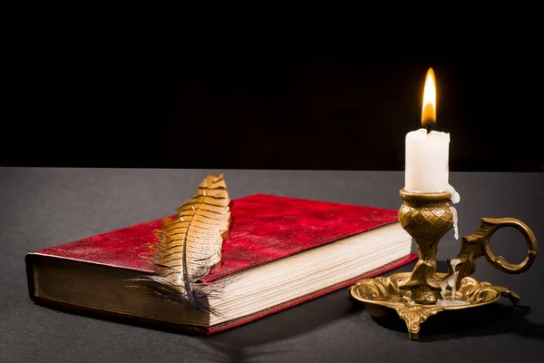 Una pluma en un libro, y una vela encendida en un candelero — Foto de Stock