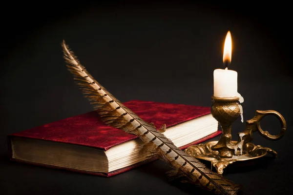 Una pluma en un libro, y una vela encendida en un candelero — Foto de Stock