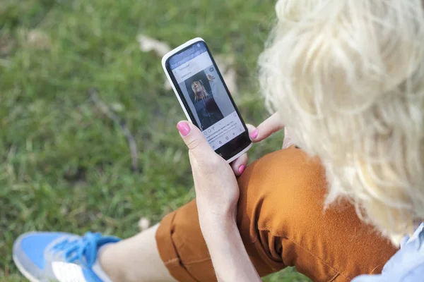 Makieta obrazu ręki trzymającej czarny telefon komórkowy z pusty ekran biały na biodra z białe trampki na trawie — Zdjęcie stockowe