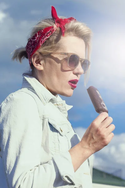 Beautiful blonde with red lips eating chocolate ice cream outdoors