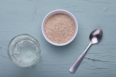 Beyaz tabakta bir yığın psyllium kabuğu ve bir bardak su. Psyllium kabuğu (ayrıca isabgol olarak da bilinir) Hindistan 'da bulunan Bitki yumurtası bitkisinin tohumlarından türetilmiş liftir. Seçici odak.