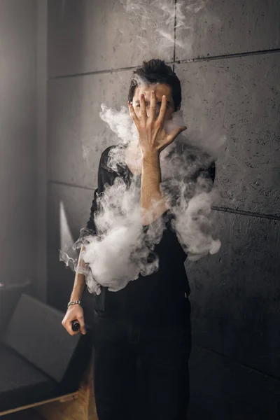 Vaping man holding a mod. A cloud of vapor. Black background. — Stock Photo, Image