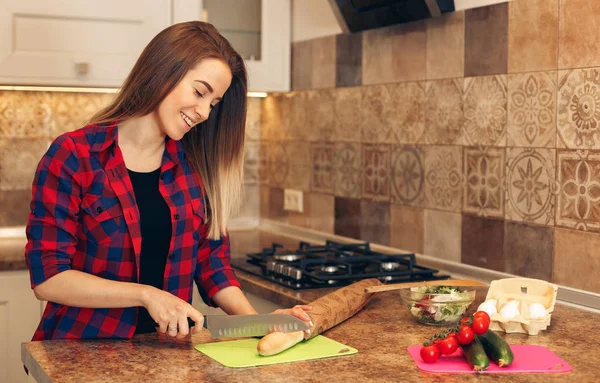 Mujer joven cortando pan en la cocina — Foto de Stock