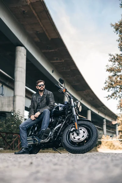 Männlicher Biker in Lederjacke auf einem Motorrad in der Nähe der Brücke — Stockfoto