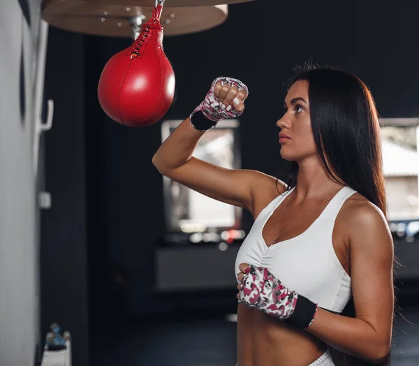 Beautiful female punching a boxing pear at the gym