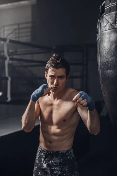 El joven ejercita una patada en el saco de boxeo en el gimnasio —  Fotos de Stock