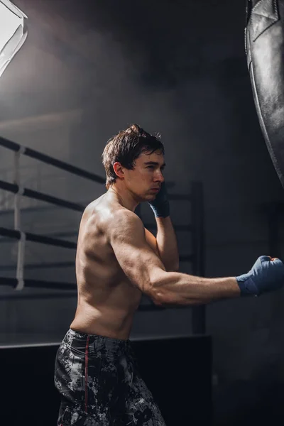 Joven deportista en entrenamiento de boxeo con un saco de boxeo —  Fotos de Stock