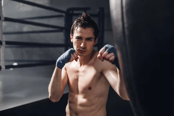 Portarait de joven boxeador en envolturas de boxeo con saco de boxeo —  Fotos de Stock