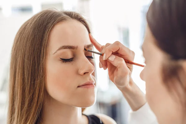 Beautiful woman drawing a shape of eyebrows using brush pencil