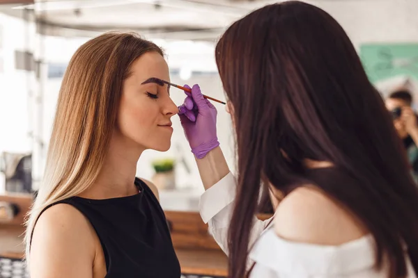 Makeup artist applies paint henna on eyebrows in a beauty salon