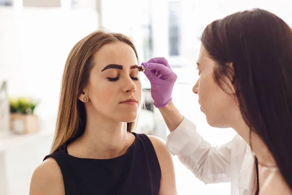 Porträt einer jungen Frau beim Bemalen ihrer Augenbrauen im Salon — Stockfoto