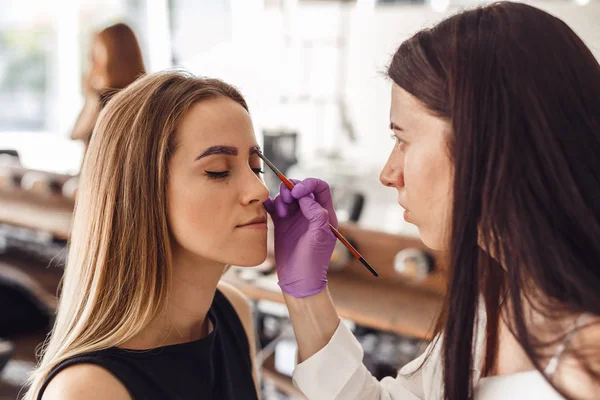 Portrait of professional cosmetologist in purple gloves making permanent eyebrows — Stock Photo, Image