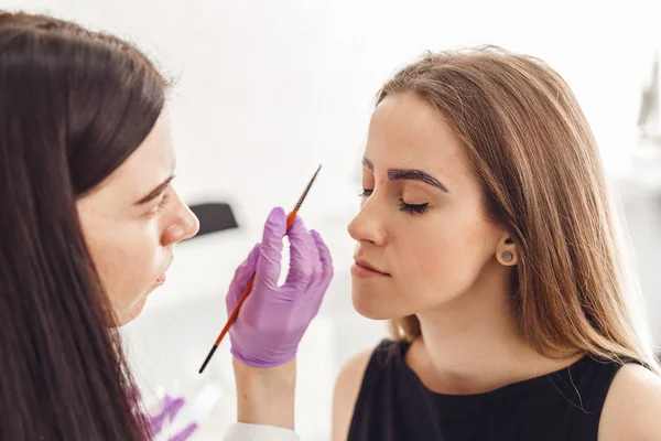 Porträt eines professionellen Kosmetikers mit lila Handschuhen, der dauerhafte Augenbrauen macht — Stockfoto