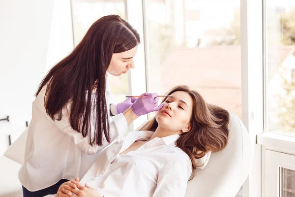 Female customer is lying on a white couch during correction and eyebrow styling.