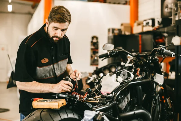 Selbstbewusster junger Mann repariert Motorrad in Werkstatt - Elektronik reparieren. — Stockfoto