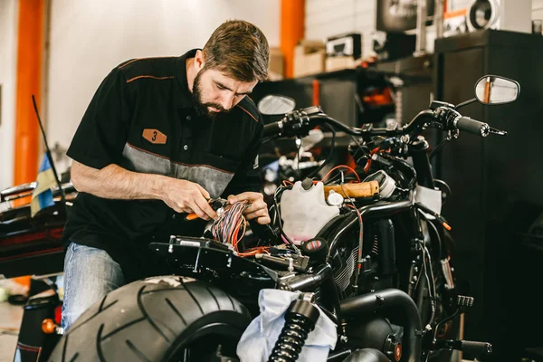 Professional motorcycle mechanic works with electronics, cuts wires.