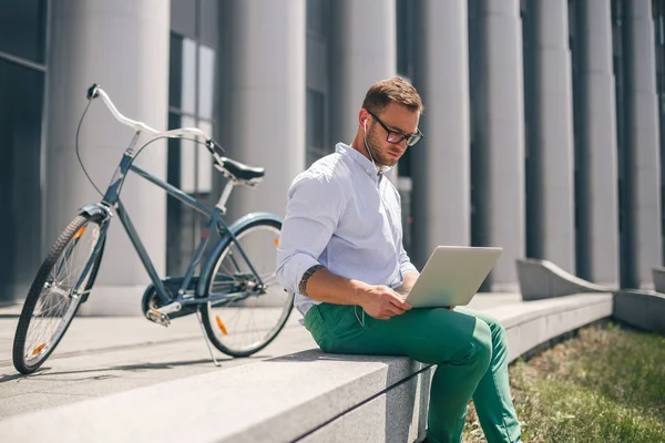 Genç adam şehir sokak üstünde laptop çalışma kulaklık.