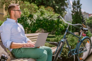 Genç bir adam bir bankta oturan ve bir dizüstü bilgisayar üzerinde çalışan