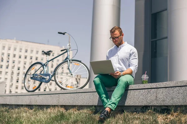 Handsome employee sitting on stairs and typing on laptop