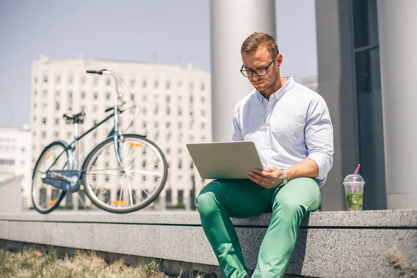 Schöner Angestellter sitzt auf der Treppe und tippt auf dem Laptop — Stockfoto