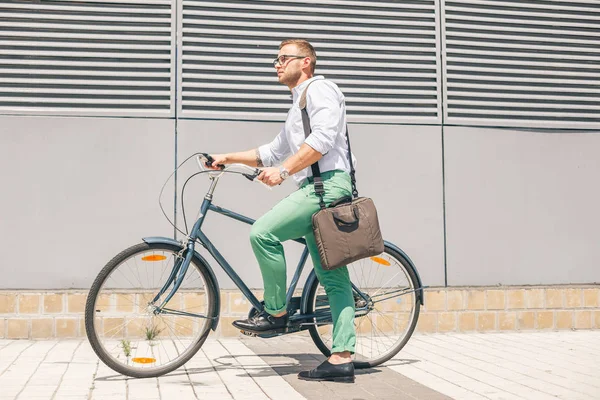 stylish businessman going to work by bike with laptop bag on shoulder