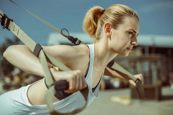 Retrato de jovem mulher atraente faz treinamento de suspensão com tiras de fitness — Fotografia de Stock
