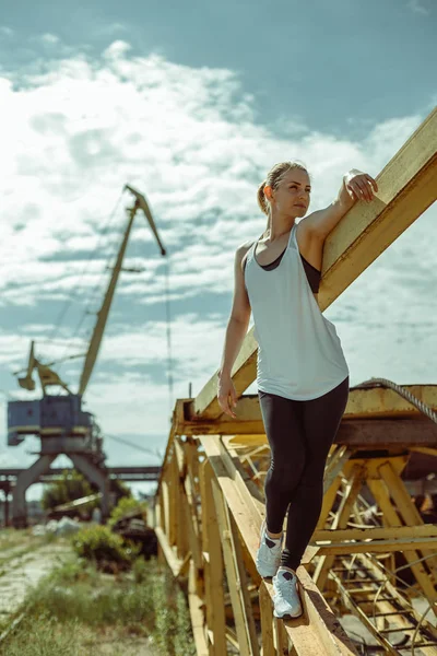 Красива жінка в спортивній формі позує на тлі морського порту — стокове фото