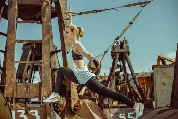 Vista lateral de la hermosa mujer joven haciendo embestidas con tiras trx — Foto de Stock