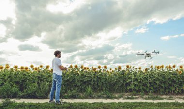 Genç adam izliyor ve açık mavi gökyüzünde uçan bir dron gezinme