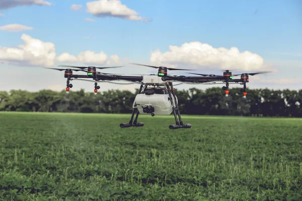Professional large drone spray water over a green field.