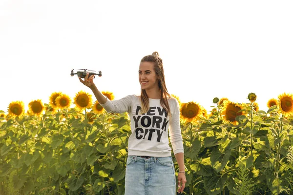 Hermosa mujer sostiene un mini dron en el fondo de un campo de girasoles . — Foto de Stock