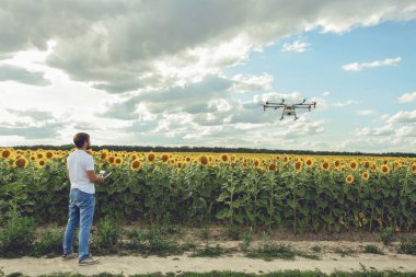 Genç adam izliyor ve açık mavi gökyüzünde uçan bir dron gezinme