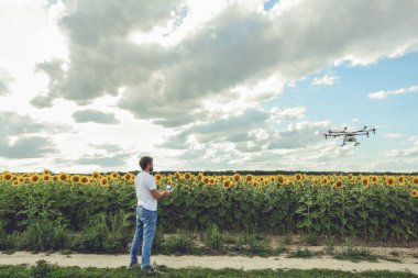 Genç adam izliyor ve açık mavi gökyüzünde uçan bir dron gezinme