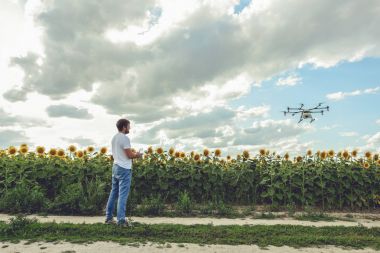 Genç adam izliyor ve açık mavi gökyüzünde uçan bir dron gezinme