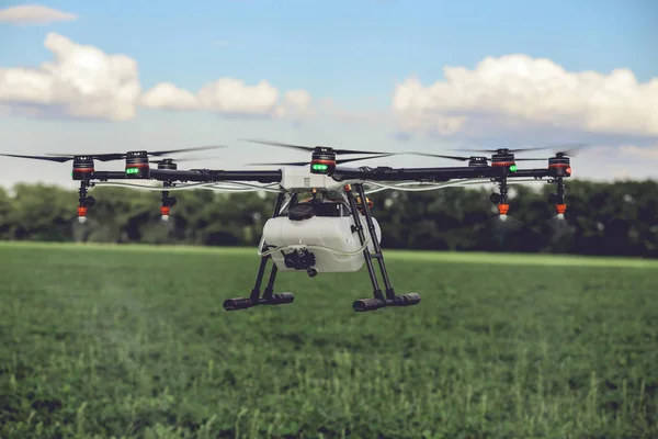 Professional large drone spray water over a green field.