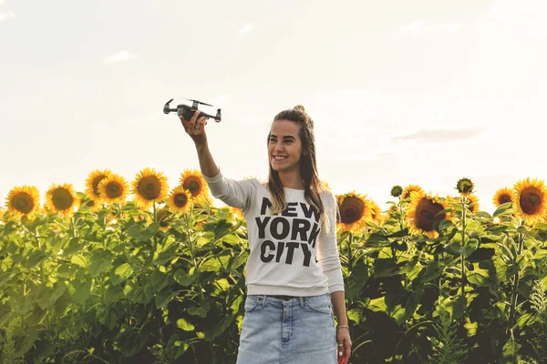 Hermosa mujer sostiene un mini dron en el fondo de un campo de girasoles . — Foto de Stock