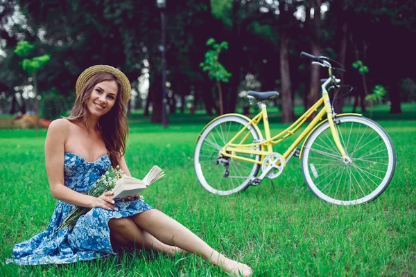 Красивый портрет молодой женщины, читающей книгу с велосипедом в парке . — стоковое фото