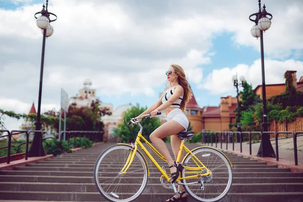 Jovem mulher hipster bonita em shorts brancos, estilo de tendência de verão perto da praia, andar de bicicleta — Fotografia de Stock