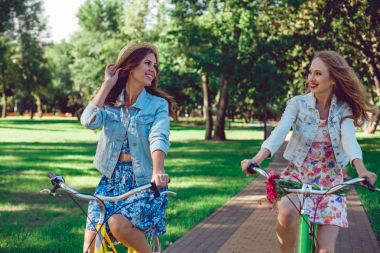 İki genç bayan arkadaşlar parkta onların bisiklet sürme.