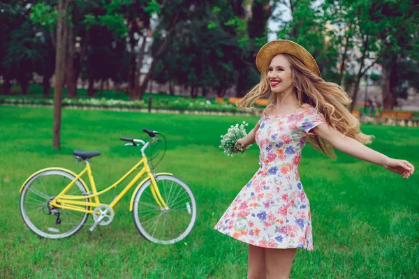 Hermosa mujer rubia en un sombrero de paja en un césped con flores giros y bailes en el parque . — Foto de Stock