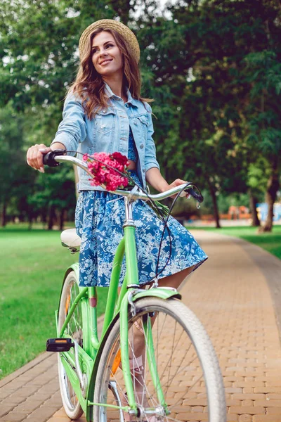 Retrato de la joven feliz sonriente montando una bicicleta en el parque . — Foto de Stock