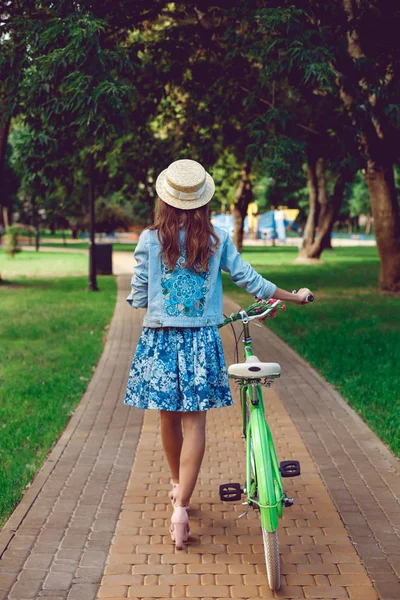 Vista desde la parte posterior de una hermosa mujer va con una bicicleta retro . — Foto de Stock