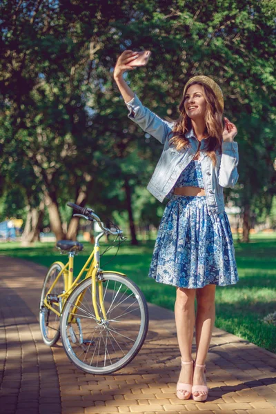 Piękna młoda kobieta w niebieskiej sukience i słomkowy kapelusz robi selfie za pomocą smart telefonu — Zdjęcie stockowe