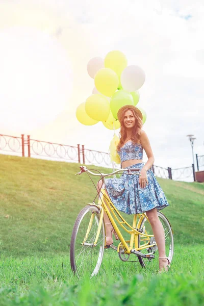 Счастливая девушка позирует на желтом велосипеде с шариками и улыбается . — стоковое фото