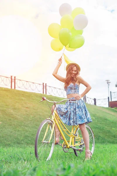 Chica feliz posando en bicicleta amarilla con globos y sonriendo . — Foto de Stock